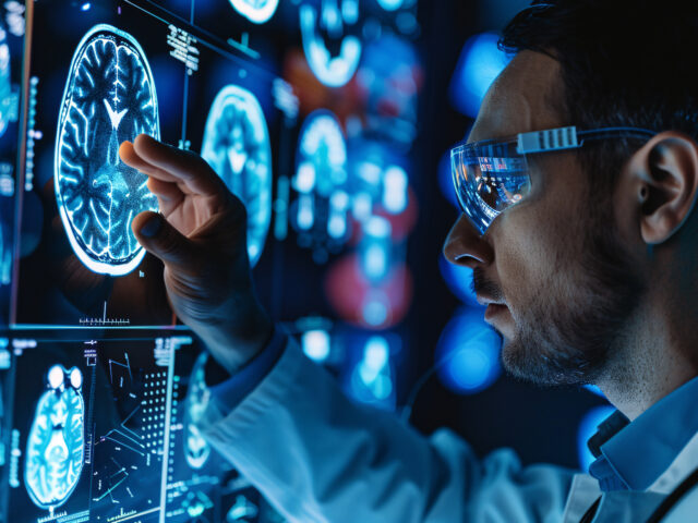 A man in a lab coat is looking at a computer screen with a picture of a brain
